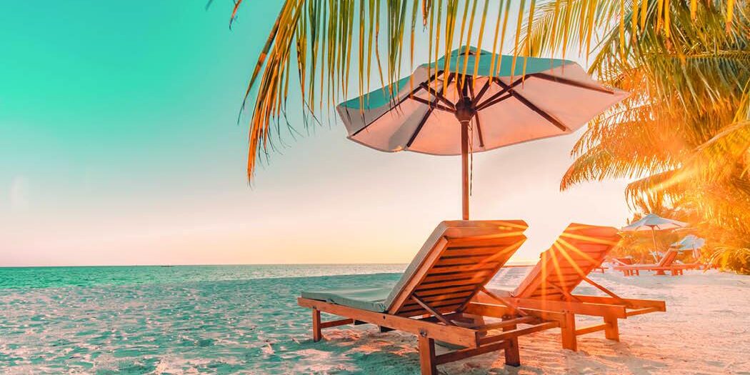 sun rising on beach with two empty beach lounge chairs